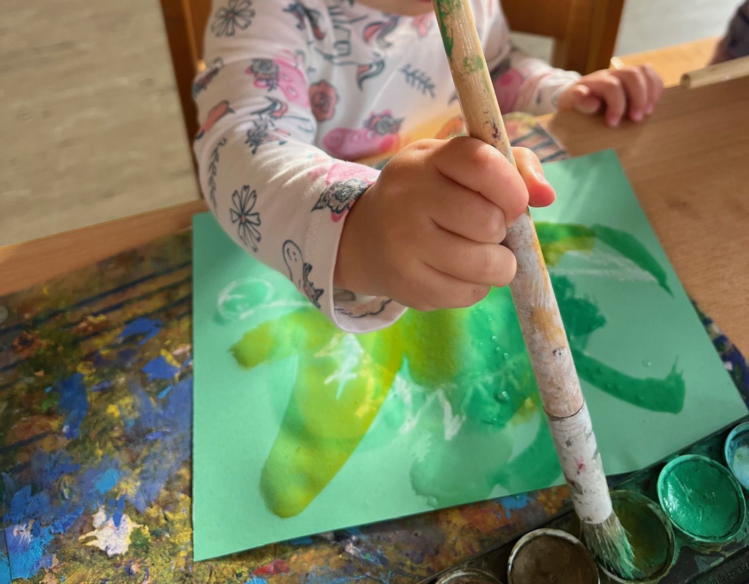 Kind malt mit einem Pinsel auf grünem Papier
